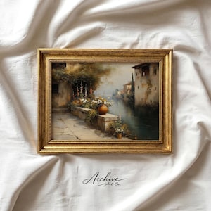 Puede incluir: Pintura de paisaje enmarcada con un marco dorado. La obra representa una escena junto al agua con edificios, un muro de piedra y flores. La pintura tiene una estética vintage, con colores suaves y pinceladas. El texto "Archive Art Co." está en la esquina inferior izquierda.