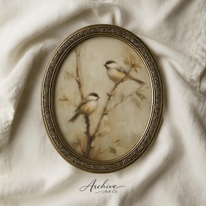 May include: An oval-shaped framed artwork featuring two small birds perched on branches. The birds have black caps and light-colored bodies. The frame is gold-toned with an ornate design. The artwork is set against a neutral background.