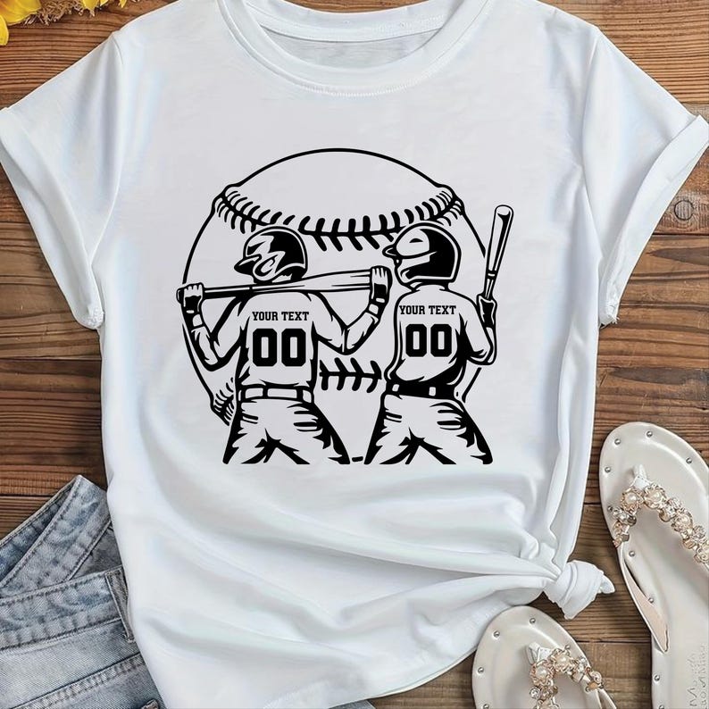 May include: White t-shirt with a black graphic of two baseball players with helmets and bats, set against a baseball. The text "YOUR TEXT" and the number "00" are on the players' uniforms. The shirt is on a wooden surface.