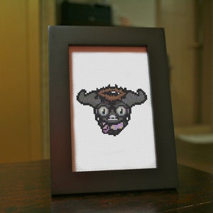 May include: A framed cross-stitch of a black and gray creature with a halo, wearing glasses and a purple bow tie.