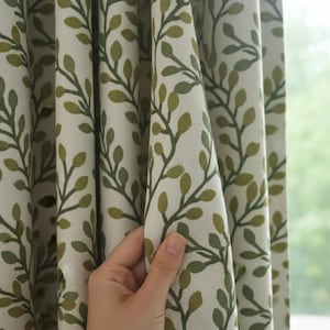 Könnte beinhalten: Vorhänge mit einem sich wiederholenden Muster aus grünen Blättern und Stielen auf cremefarbenem Hintergrund. Der Stoff wird offen gehalten, wodurch das Design und die Textur sichtbar werden. Geeignet für die Inneneinrichtung.