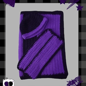 May include: A handmade crochet baby set in purple and navy blue. The set includes a beanie, a blanket, and a matching pair of booties. The Plaid Heart Baby Co. logo is in the bottom left corner. The set is displayed on a gray background.