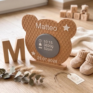Könnte beinhalten: Eine hellbraune, bärenförmige Holztafel mit Wabenstruktur. Sie zeigt den Namen Matteo, zwei weiße Sterne und eine graue kreisförmige Mitte mit der Uhrzeit 10:15, dem Gewicht 3620g, der Länge 52cm und dem Datum 23.07.2028 in weißer Schrift.
