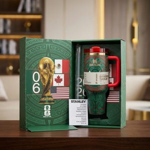 Puede incluir: Un juego de vasos Stanley Quencher verde y rojo en una caja de regalo. El vaso presenta un asa y tapa rojas, con un dise&ntilde;o de inspiraci&oacute;n azteca verde y rojo. La caja incluye una pajita y un trofeo dorado de la Copa Mundial de la FIFA.