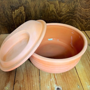 May include: A round, light orange terracotta bowl with a matching lid. The bowl features subtle horizontal ridges along its exterior side, and the lid has a smooth, slightly recessed center with the embossed text "BERTORI" visible.
