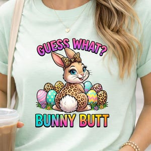 May include: A light green t-shirt featuring a cartoon bunny with a leopard print design, surrounded by Easter eggs. The text "GUESS WHAT?" and "BUNNY BUTT" are displayed in colorful, playful fonts.