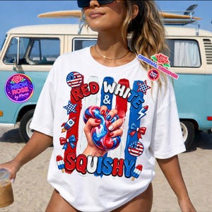 Könnte beinhalten: Weißes T-Shirt mit einem patriotischen Design mit den Worten "Red, White & Squishy". Das Design umfasst rote, weiße und blaue Elemente, eine Hand, die ein Squishy-Spielzeug drückt, und Akzente der amerikanischen Flagge. Das Shirt hat einen Rundhalsausschnitt.