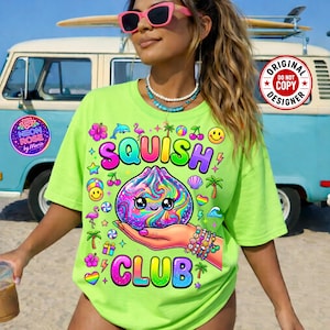 Può includere: Una maglietta verde neon con le parole "SQUISH CLUB" in un gradiente arcobaleno. La maglietta presenta una grafica colorata di un giocattolo squishy tenuto in mano, circondato da icone come palme, ciliegie e faccine.