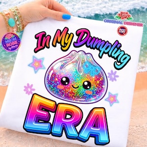Puede incluir: Funda de almohada blanca con un gráfico colorido que dice "In My Dumpling ERA". El diseño presenta una bola de masa kawaii con un relleno de purpurina arcoíris, rodeada de estrellas y flores. El texto y los gráficos tienen un esquema de color degradado vibrante.