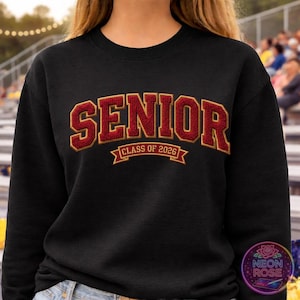 May include: Black sweatshirt with the word "SENIOR" in red and gold lettering. Below the word "SENIOR" is the text "CLASS OF 2026" in a banner design. The sweatshirt is a classic crew neck style.