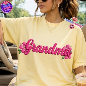 May include: A light yellow t-shirt with the word "Grandma" in a vibrant pink, adorned with pink hibiscus flowers and green leaves. The shirt features the "Neon Rose by Maria" and "Original Designer" logos.
