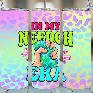May include: Three stainless steel tumblers with a vibrant design. The design shows a hand squeezing a green and blue stress ball, with the words "IN MY NEEDOH ERA". The background has a leopard print pattern in pastel colours.