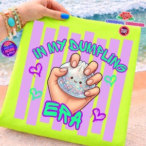 May include: A neon green pillow with vertical purple stripes and the text "IN MY DUMPLING ERA" in green and pink. The pillow features a cartoon hand holding a dumpling with a smiling face and glitter.