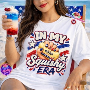 Könnte beinhalten: Weißes T-Shirt mit patriotischem Design. Das Shirt zeigt den Text "IN MY Squishy ERA" mit einer Hand, die ein Butterstück hält. Das Design enthält rote, weiße und blaue Farben, Sterne und Streifen. Die Butter ist mit "SALTED BUTTER 4 OZ" beschriftet.