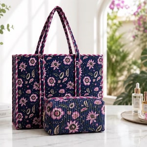 May include: A quilted tote bag and a matching rectangular zippered pouch, both featuring a dark navy blue fabric base with a repeating floral pattern in shades of pink, white, and green, finished with pink and white striped piping trim.