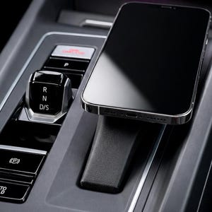 Peut inclure: Un smartphone noir est posé sur un support de téléphone noir dans la console d'une voiture. La console comprend des commandes de changement de vitesse, dont Park, Marche arrière, Neutre et D/S, ainsi qu'un bouton Auto Hold.