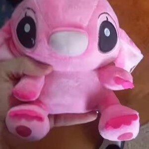 May include: A pink plush toy with large black eyes, a white muzzle, and large ears. The toy has pink accents on its hands and feet. The toy is held in a person's hand.