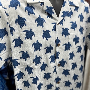 May include: White button-down shirt with a blue and white pattern of sea turtles. The shirt has a classic collar and short sleeves.