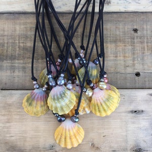 May include: A group of necklaces featuring yellow, pink, and orange seashells with black cords and pearl accents.