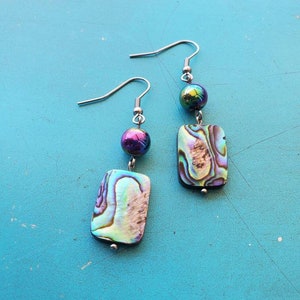 May include: A pair of iridescent abalone shell earrings with silver hooks and iridescent purple beads.