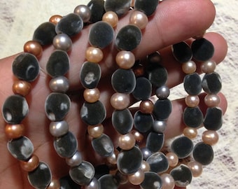 May include: Five strands of gray, brown, and pink beaded bracelets. The beads are oval shaped and have a velvety texture.
