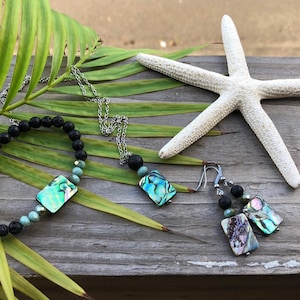 May include: A set of jewelry featuring abalone shell and lava rock beads. The set includes a necklace, bracelet, and earrings. The necklace and earrings have silver chains.