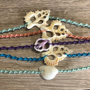 May include: Five colorful macrame bracelets with different seashells attached. The bracelets are made with a variety of colors, including green, blue, purple, orange, and white. The seashells are all different shapes and sizes, and some have intricate designs.