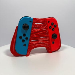 May include: A custom red and blue Nintendo Switch Joy-Con controller grip. The left Joy-Con is blue, and the right is red. The grip is red with a textured design. The controller has black buttons and joysticks.