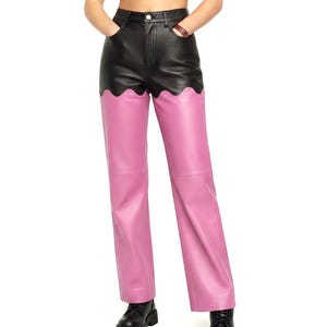 May include: High-waisted trousers featuring a two-tone design with a black upper section and pink lower section. The transition between the black and pink panels is defined by a distinct scalloped edge. The trousers include a button closure.