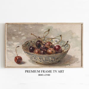 Könnte beinhalten: Gerahmter Kunstdruck eines Stilllebens mit einer Schale Kirschen. Die Kirschen sind tiefrot und braun, die Schale hellblau mit einem dekorativen Muster. Der Text "PREMIUM FRAME TV ART" befindet sich unten.