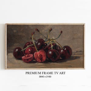 Könnte beinhalten: Gerahmtes Stillleben mit Kirschen. Die dunkelroten Kirschen sind zusammengefasst, einige ganz und andere halbiert, wodurch ihr saftiges Inneres sichtbar wird. Das Gemälde hat eine Vintage-Ästhetik mit dem Text "PREMIUM FRAME TV ART" darunter.