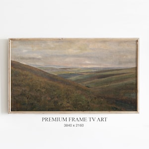 Pode incluir: Pintura de paisagem emoldurada retratando colinas onduladas em tons de verde e marrom sob um céu nublado. A obra de arte é apresentada em uma moldura de madeira clara. O texto na parte inferior diz "PREMIUM FRAME TV ART" e as dimensões.