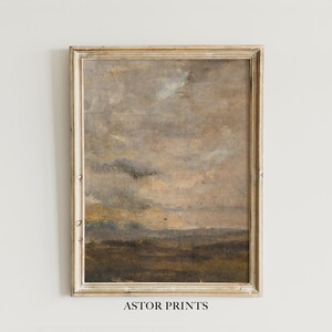 Könnte beinhalten: Gerahmtes Landschaftsgemälde mit gedämpften Farben. Das Kunstwerk zeigt einen bewölkten Himmel über einem Feld, mit Brauntönen, Grau und Beige. Der Rahmen ist hellgoldfarben und leicht verwittert. Der Text "ASTOR PRINTS" befindet sich unten.
