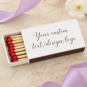 May include: A rectangular white matchbox with a sliding tray containing wooden matches with red tips. The top of the box features the black printed text: Your custom text/design/logo. The box has dark brown sides and is partially open to reveal the matches.