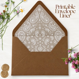 Puede incluir: Un sobre de papel marrón con un forro imprimible que presenta un patrón de cachemira blanco. El texto "Printable Envelope Liner" aparece en la esquina superior derecha. El sobre está abierto, mostrando el diseño decorativo interior.