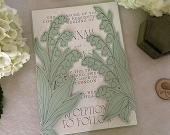 Pode incluir: Um convite de casamento retangular com duas ilustrações recortadas de lírios do vale em verde claro nos lados esquerdo e direito. O cartão branco exibe texto impresso em preto, incluindo as palavras, The pleasure of your company is requested at the wedding of, e Reception to follow.