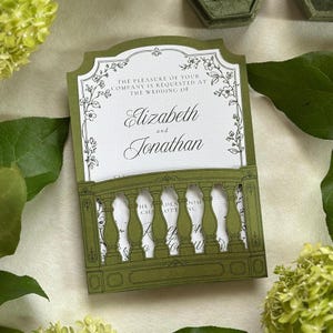 May include: A white wedding invitation card with black text reading The pleasure of your company is requested at the wedding of Elizabeth and Jonathan, framed by a die-cut olive green cardstock overlay featuring a decorative balustrade design.