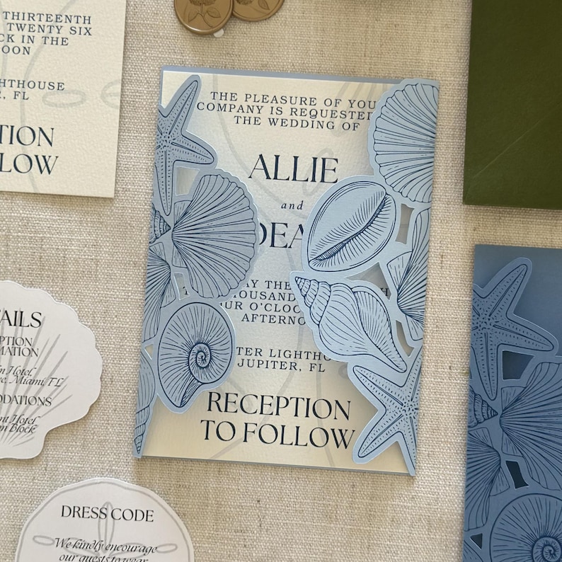 Pode incluir: Um conjunto de convites de casamento com uma capa dobr&aacute;vel azul-clara cortada a laser, decorada com ilustra&ccedil;&otilde;es de conchas e estrelas-do-mar. O cart&atilde;o interno exibe texto em preto com os nomes Allie e Dean, al&eacute;m de outros itens de papelaria a condizer.