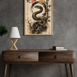 Könnte beinhalten: Ein gerahmter Kunstdruck mit einer schwarz-goldenen Schlange, die sich im Kreis windet, vor einem cremefarbenen Hintergrund mit einer roten Sonne, Bambusstangen und japanischen Schriftzeichen, darunter das Kanji für Schlange, 蛇, oben links.