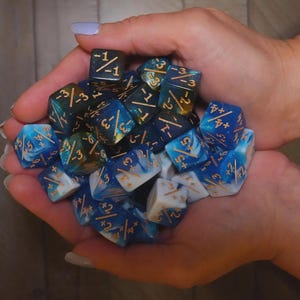 Può includere: Un pugno di dadi poliedrici di varie forme e dimensioni. I dadi sono principalmente blu e bianchi con numeri dorati. Alcuni dadi hanno un effetto marmorizzato, mentre altri sono a tinta unita. Questi dadi sono usati per giochi da tavolo.