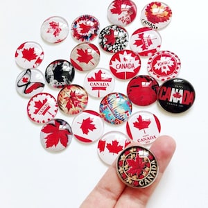May include: A collection of round glass cabochons featuring various Canadian-themed designs, including red maple leaves, the text Canada, and Happy Canada Day. The circular pieces display diverse patterns such as butterflies, cityscapes, and floral motifs.