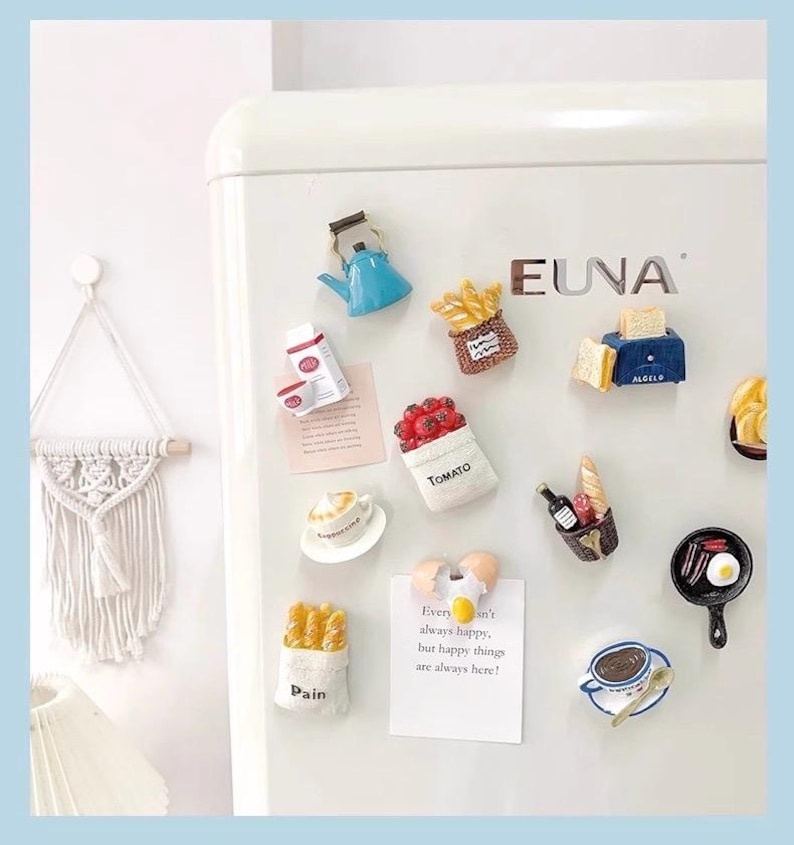 May include: A collection of colorful refrigerator magnets in various food shapes, including a blue teapot, a basket of fries, a tomato bag, a toaster, and a cup of coffee. A note says "Every isn't always happy, but happy things are always here!"