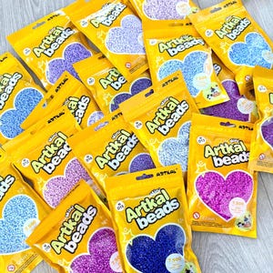Könnte beinhalten: Eine Ansammlung gelber Artkal Beads-Packungen, die jeweils ein herzförmiges Design mit farbenfrohen Mini-Perlen zeigen. Die Packungen enthalten 7.500 Mini-Perlen und sind für Kinder ab 12 Jahren geeignet.