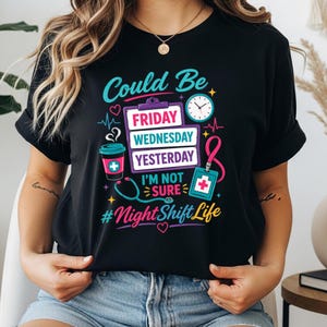 May include: A black t-shirt featuring a colourful graphic with a clipboard listing Friday, Wednesday, and Yesterday, a coffee cup, a clock, a stethoscope, and an ID badge. The text reads Could Be, I'M NOT SURE, and #NightShiftLife in bright colours.