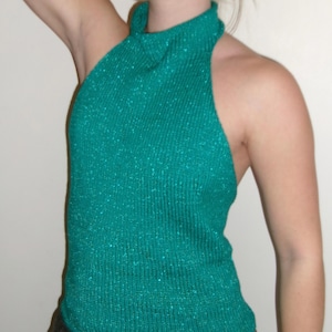 Könnte beinhalten: Ein tealfarbenes Neckholder-Top mit gerippter Textur und dezentem Glitzer. Das Top hat einen hohen Ausschnitt und ein ärmelloses Design. Der Stoff scheint ein Strickmaterial zu sein. Das Kleidungsstück ist einfarbig.