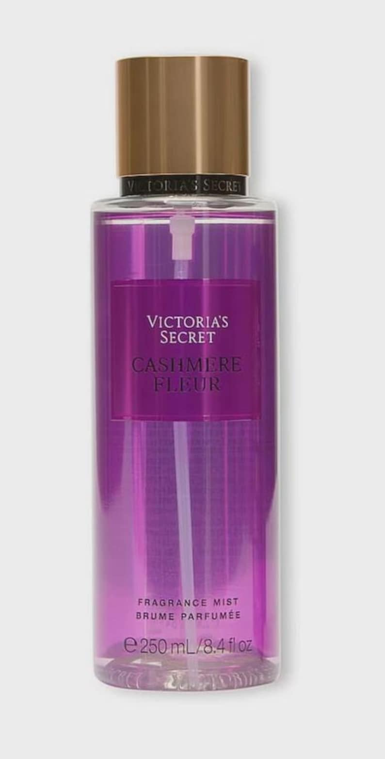 Op de afbeelding: Een hoge, transparante fles Victoria's Secret Cashmere Fleur geurmist. De fles heeft een gouden dop en een paarse vloeistof. Het etiket toont de merknaam en productnaam. Bevat 250 ml.