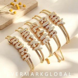 May include: Five gold-tone adjustable bracelets featuring names spelled out in pavé-set clear crystals. The names displayed are LAURA, JACKY, ELLIE, RINA, and KAY. Each bracelet has a delicate box chain design with a sliding clasp mechanism.