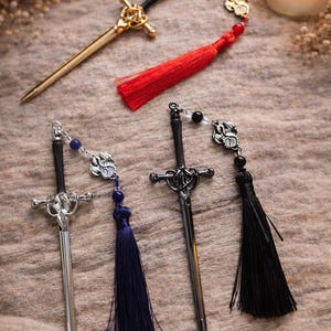 May include: Three sword-shaped bookmarks with black handles and metallic blades. One is gold with red beads and a red tassel, one is silver with blue beads and a blue tassel, and one is black with black beads and a black tassel, each featuring a dragon charm.