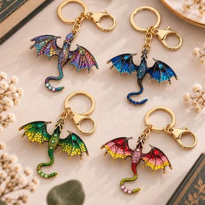 May include: Four metal dragon keychains with gold-tone hardware and lobster clasps. Each dragon features intricate enamel detailing in vibrant colour combinations including purple, blue, green, and red, accented with small embedded crystals.