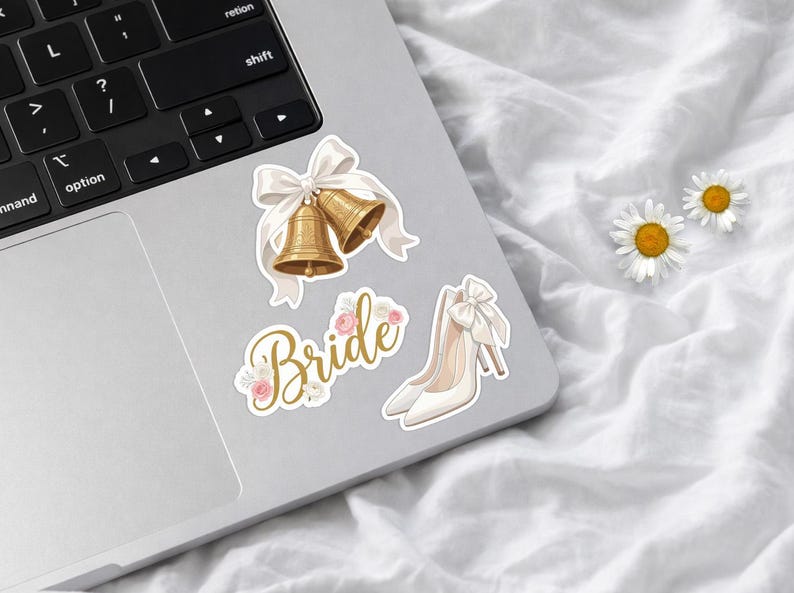 May include: A set of three stickers featuring two gold wedding bells tied with a white ribbon, the word Bride in gold cursive script decorated with small pink and white flowers, and a pair of white high-heeled shoes with a white bow.